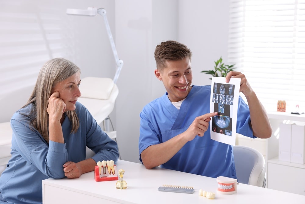 Doctor,Showing,Teeth,Scan,And,Dental,Implant,Models,To,Senior